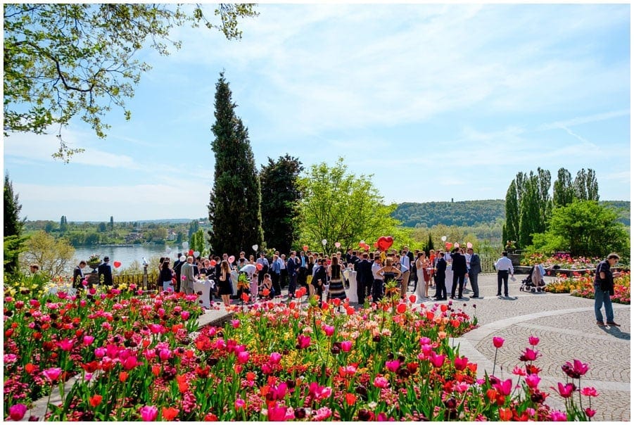 Hochzeitsgäste mit vielen Blumen im Vordergrund.