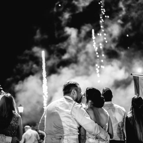 Das Brautpaar küsst sich vor dem Feuerwerk im Hintergrund.